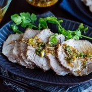 A dark plate containing sliced steamed pork topped with garlic soy sauce and garnished with cilantro.