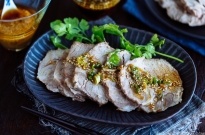 A dark plate containing sliced steamed pork topped with garlic soy sauce and garnished with cilantro.