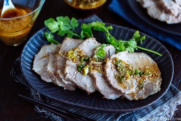 A dark plate containing sliced Pressure Cooker Steamed Pork topped with garlic soy sauce and garnished with cilantro.