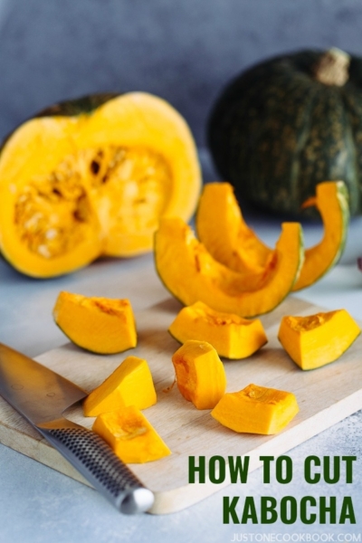 A whole Kabocha squash is being peeled and cut into cubes on a cutting board.