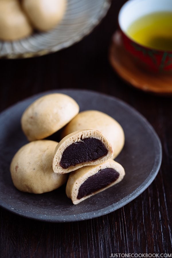 A dark Japanese plate containing manju filled with red bean paste served with green tea.