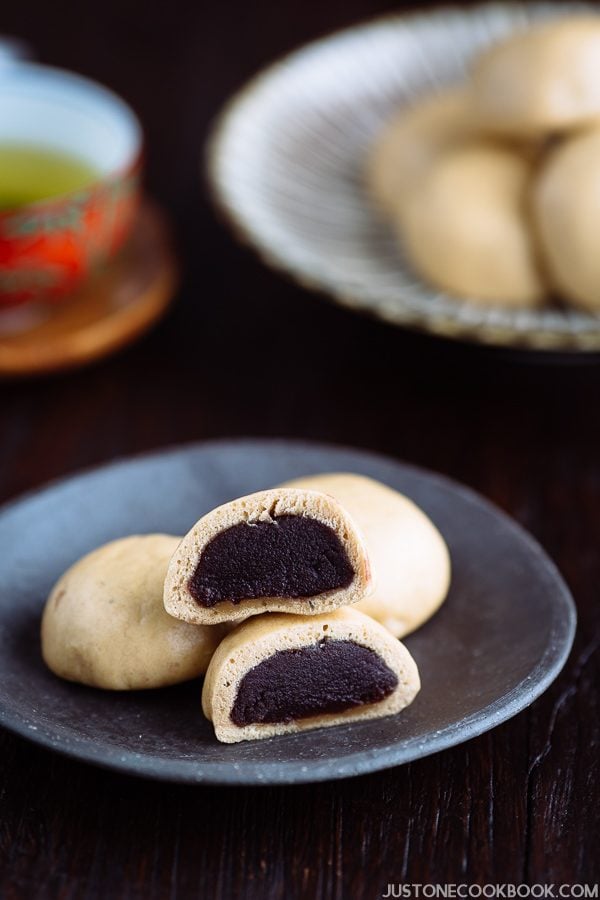 A dark Japanese plate containing manju filled with red bean paste served with green tea.