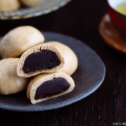 A dark Japanese plate containing manju filled with red bean paste served with green tea.