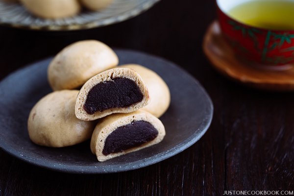 A dark Japanese plate containing manju filled with red bean paste served with green tea.