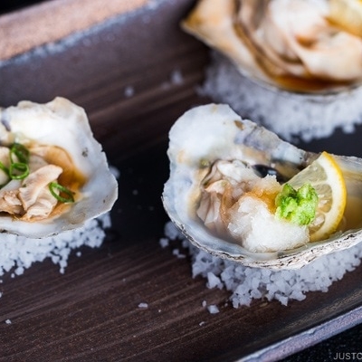 Dark Japanese plate containing Grilled Oysters with 3 kinds of garnish and Ponzu Sauce