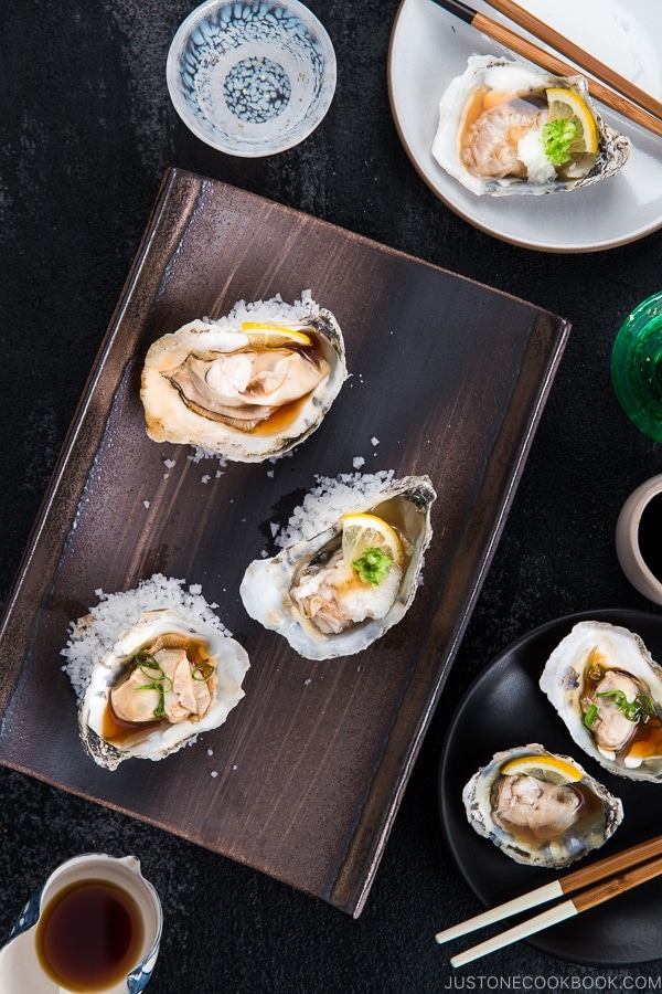 Dark Japanese plate containing Grilled Oysters with 3 kinds of garnish and Ponzu Sauce