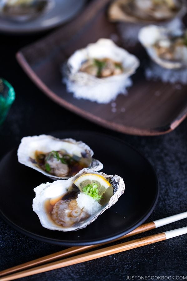 Dark Japanese plate containing Grilled Oysters with 3 kinds of garnish and Ponzu Sauce