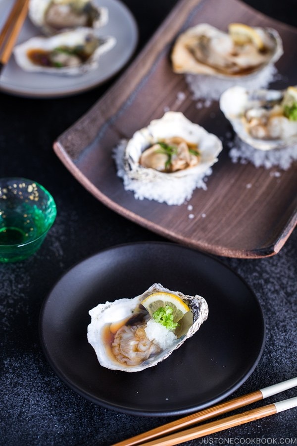 Dark Japanese plate containing Grilled Oysters with 3 kinds of garnish and Ponzu Sauce