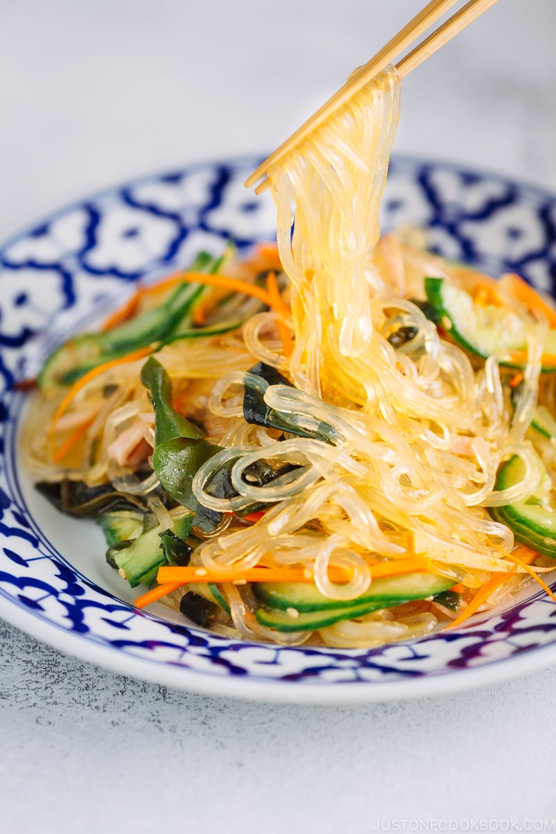 Chopsticks holding glass noodles being pulled out from the delicious Harusame Salad (Japanese Glass Noodle Salad) on a blue and white plate.