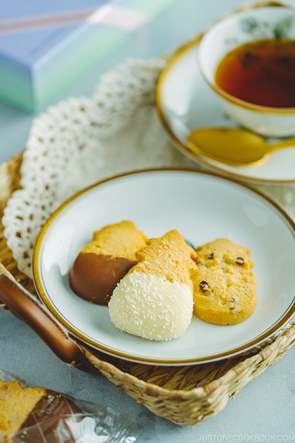 Tea in a cup and a gold rim dish containing various cookies from Honolulu Cookie Company.