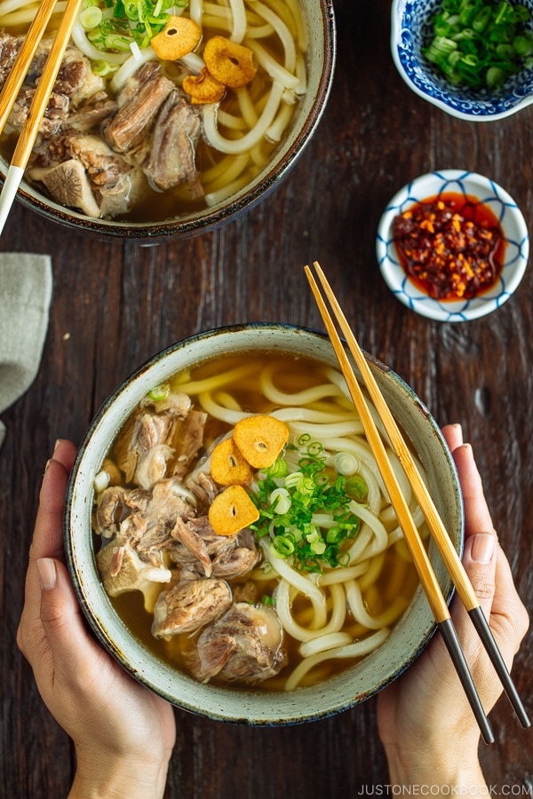 A large bowl of Oxtail Udon topped with tender meat, fried garlic, and green onion.