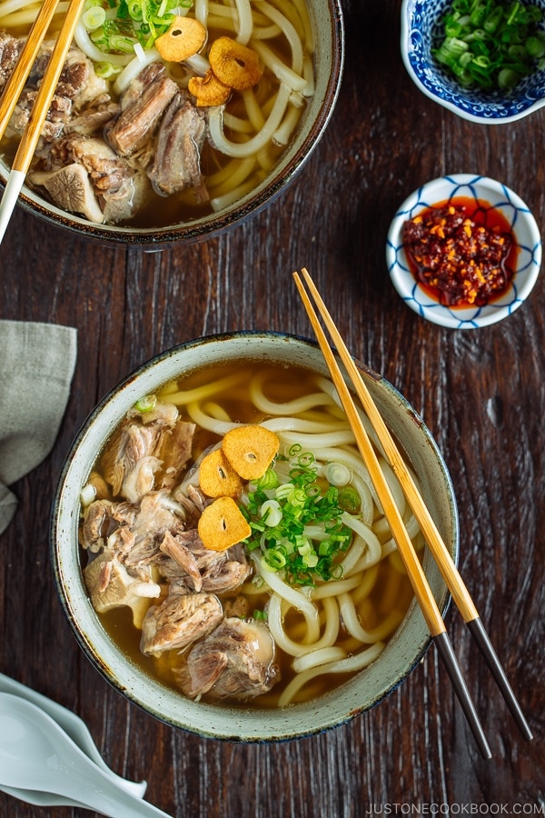 A large bowl of Oxtail Udon topped with tender meat, fried garlic, and green onion.