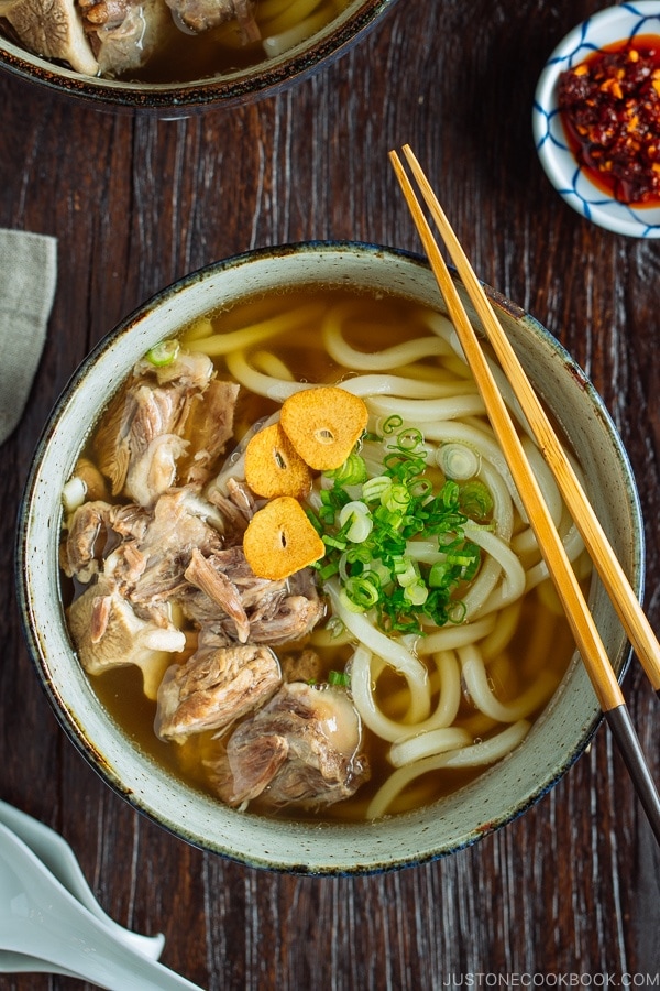 A large bowl of Oxtail Udon topped with tender meat, fried garlic, and green onion.