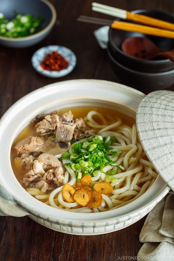 A Japanese donabe (earthenware pot) containing Oxtail Udon topped with tender meat, fried garlic, and green onion.