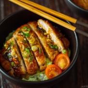 A black bowl containing Teriyaki Pork over steamed rice drizzled with homemade teriyaki glaze.