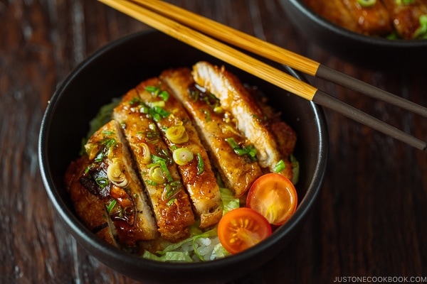 A black bowl containing Teriyaki Pork over steamed rice drizzled with homemade teriyaki glaze.