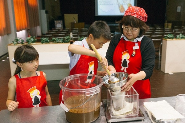 children scooping soy sauce raw mixture into bag for pressing at Kikkoman Factory in Noda Japan | justonecookbook.com