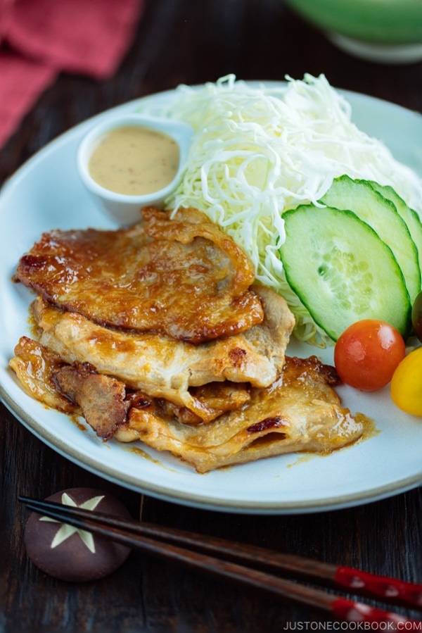 A white plate containing thinly sliced Miso Ginger Pork served with shredded cabbage, sliced cucumbers, and cherry tomatoes.