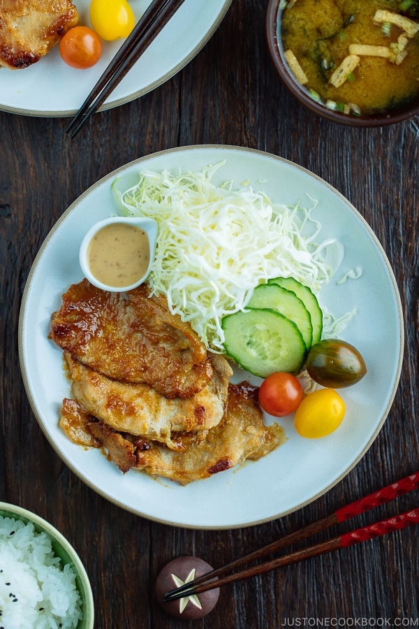 A white plate containing thinly sliced Miso Ginger Pork served with shredded cabbage, sliced cucumbers, and cherry tomatoes.