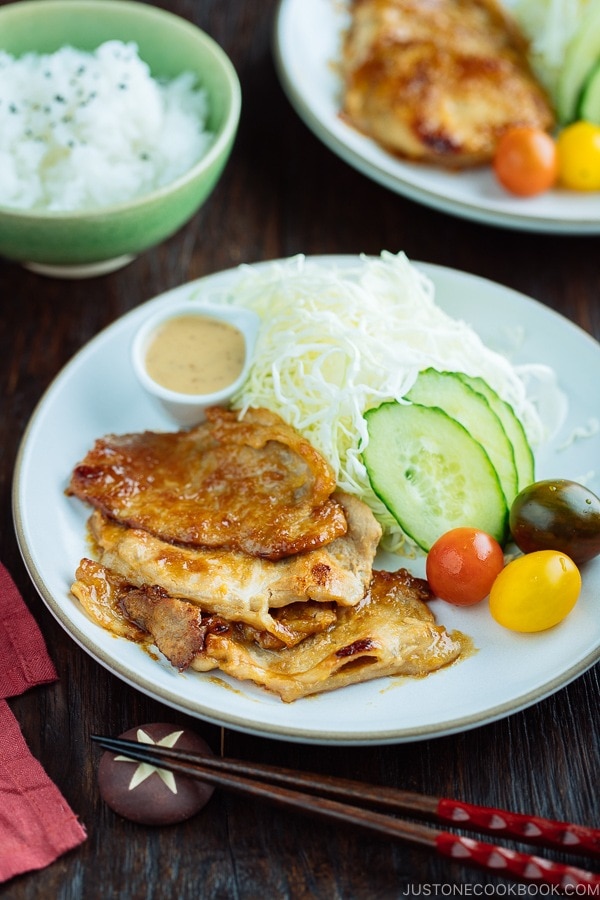 A white plate containing thinly sliced Miso Ginger Pork served with shredded cabbage, sliced cucumbers, and cherry tomatoes.