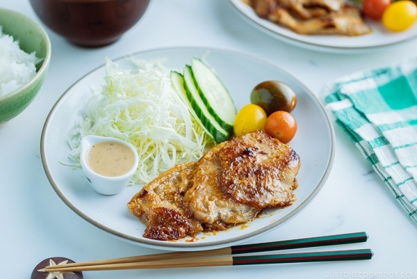 A white plate containing thinly sliced Miso Ginger Pork served with shredded cabbage, sliced cucumbers, and cherry tomatoes.