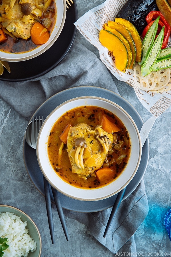 A white bowl containing soup curry with various vegetable on top.