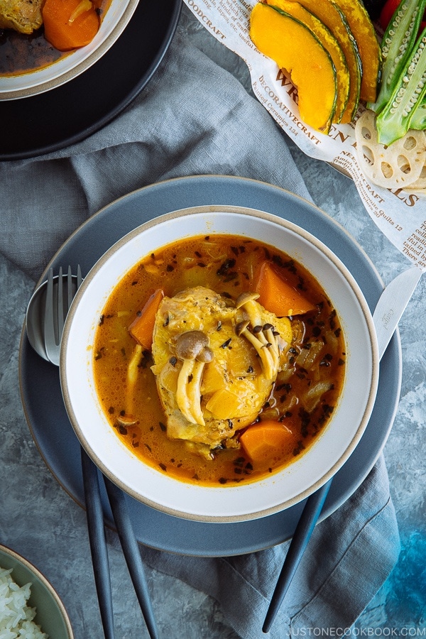 A white bowl containing soup curry with various vegetable on top.