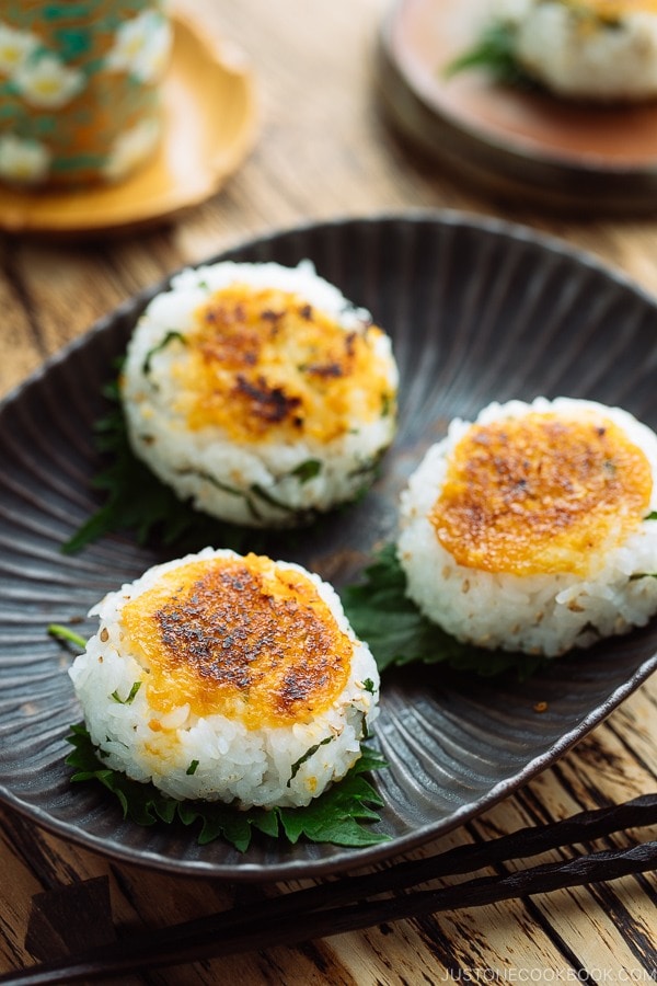 A black dish containing miso flavored Yaki Onigiri (Grilled Rice Balls) garnished with shiso leaves.