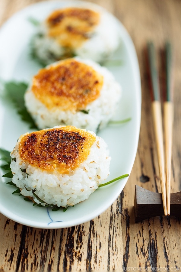 A white dish containing miso flavored Yaki Onigiri (Grilled Rice Balls) garnished with shiso leaves.
