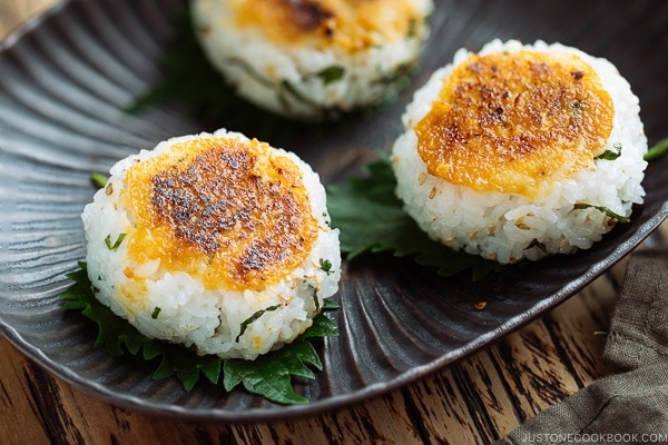 A black dish containing miso flavored Yaki Onigiri (Grilled Rice Balls) garnished with shiso leaves.