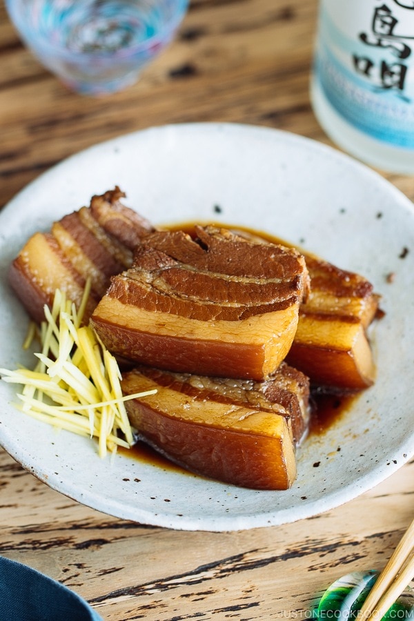 A white plate containing 3 slices of Rafute (Okinawan Braised Pork Belly) garnished with julienned ginger.