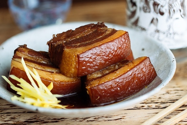 A white plate containing 3 slices of Rafute (Okinawan Braised Pork Belly) garnished with julienned ginger.