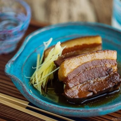 A blue plate containing 2 slices of Rafute (Okinawan Braised Pork Belly) garnished with julienned ginger.