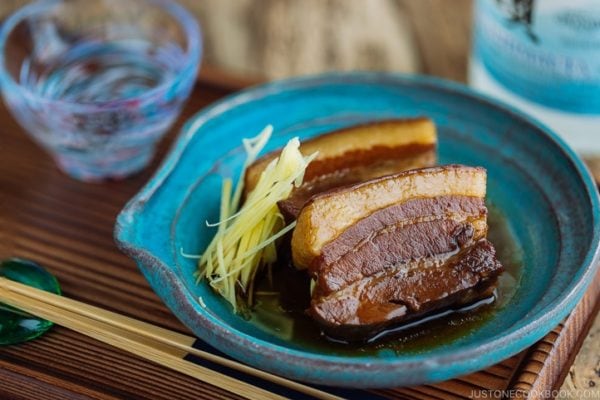 A blue plate containing 2 slices of Rafute (Okinawan Braised Pork Belly) garnished with julienned ginger.