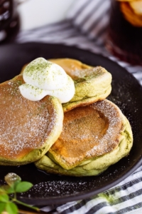 Matcha Souffle Pancakes topped with powder sugar and fresh whipped cream.