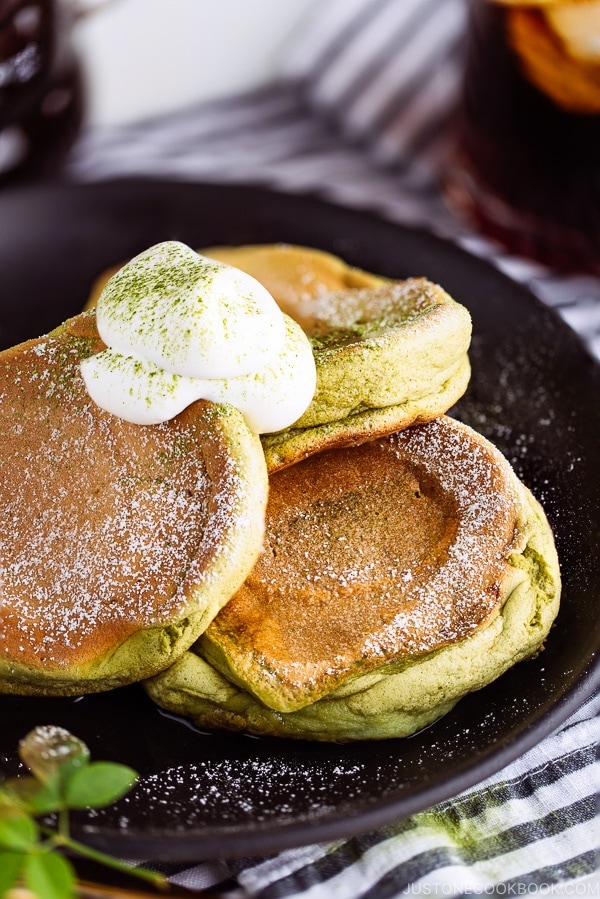 Matcha Souffle Pancakes topped with powder sugar and fresh whipped cream.