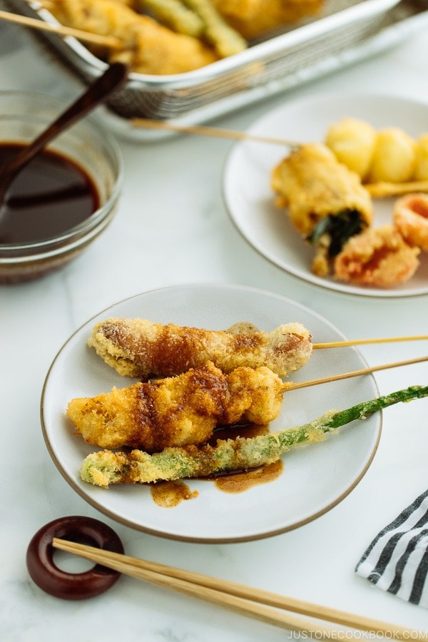 A white plate containing golden and crispy Kushikatsu (Kushiage) served with savory sauce.