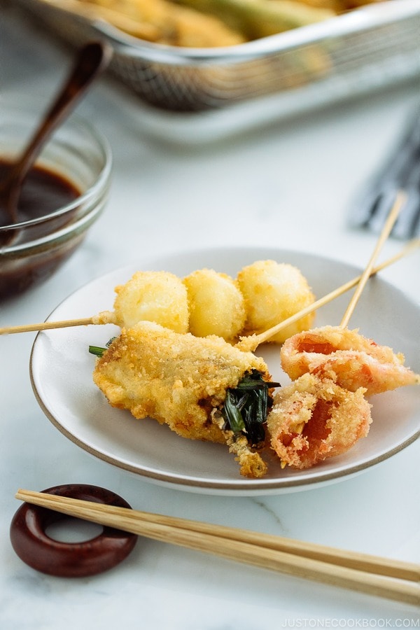 A white plate containing golden and crispy Kushikatsu (Kushiage) served with savory sauce.