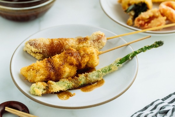 A white plate containing golden and crispy Kushikatsu (Kushiage) served with savory sauce.