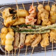 Wire basket containing golden and crispy Kushikatsu (Kushiage) served with savory sauce.