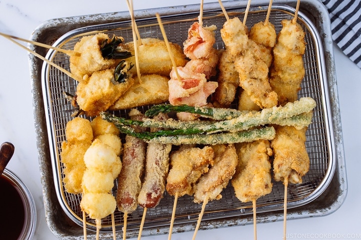 Wire basket containing golden and crispy Kushikatsu (Kushiage) served with savory sauce.