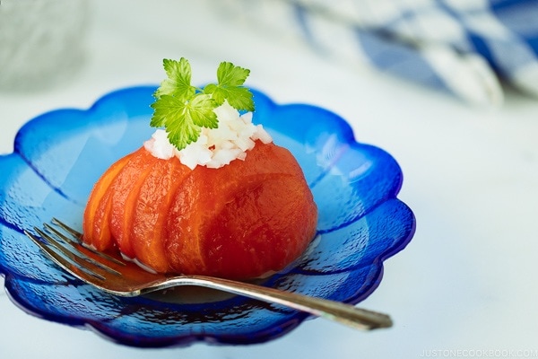 A blue glass containing Japanese-style Pickled Tomatoes garnished with minced onion.