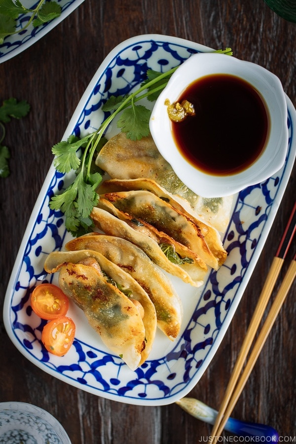 A plate containing chicken shiso gyoza and a small bowl of ponzu and yuzu kosho.