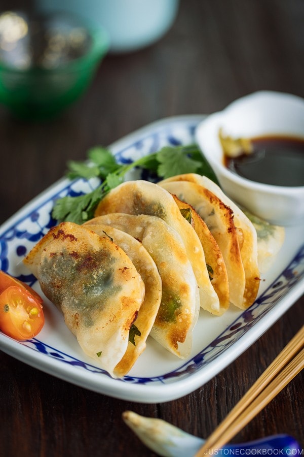 A plate containing chicken shiso gyoza and a small bowl of ponzu and yuzu kosho.
