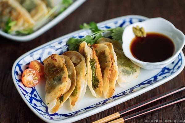 A plate containing chicken shiso gyoza and a small bowl of ponzu and yuzu kosho.