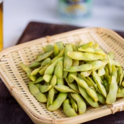 Edamame served in bamboo basket and beer glass in the back.