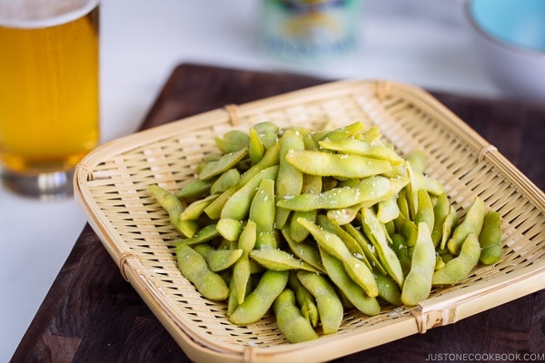 Edamame served in bamboo basket and beer glass in the back.