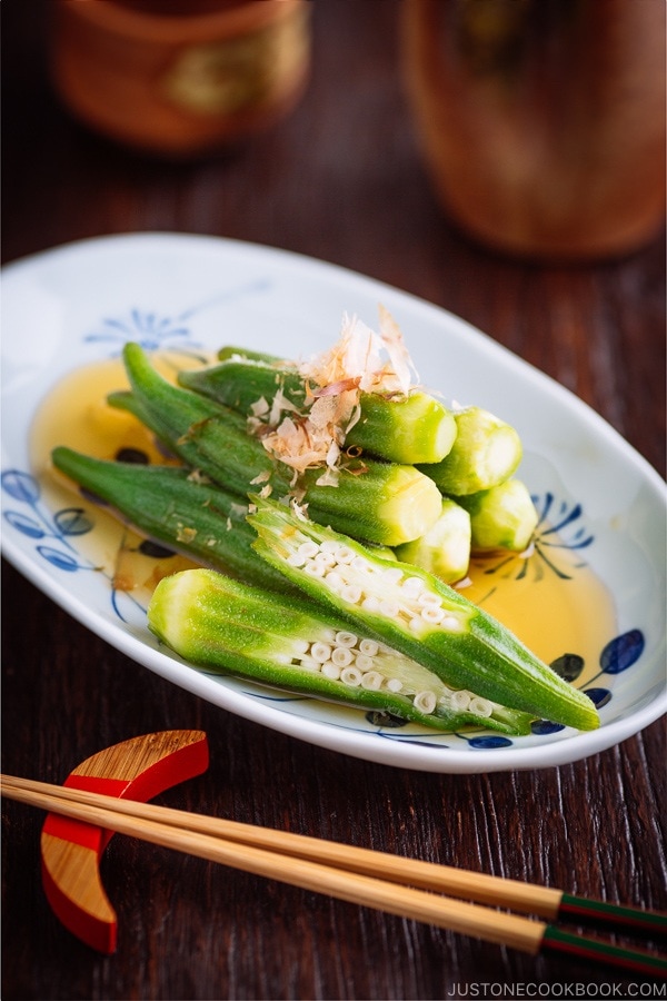 Japanese white and blue plate containing Japanese style okra salad topped with bonito flakes.