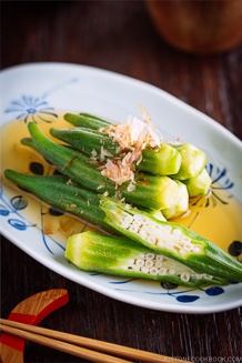 Japanese white and blue plate containing Japanese style okra salad topped with bonito flakes.
