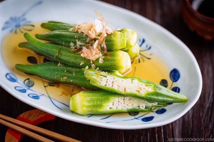 Japanese white and blue plate containing Japanese style okra salad topped with bonito flakes.
